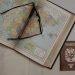 A vintage map of Spain with eyeglasses and a Venezuelan passport, symbolizing travel planning.