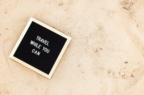 Letter board with 'Travel While You Can' message displayed on sandy beach scene, inspiring wanderlust.