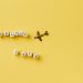 Flat lay of 'Travel Safe' text with airplane pendant on yellow background, evoking travel and safety concepts.