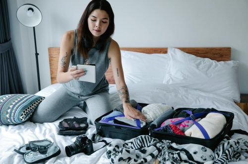 Woman sitting on bed packing a suitcase and taking notes for her travel plan.